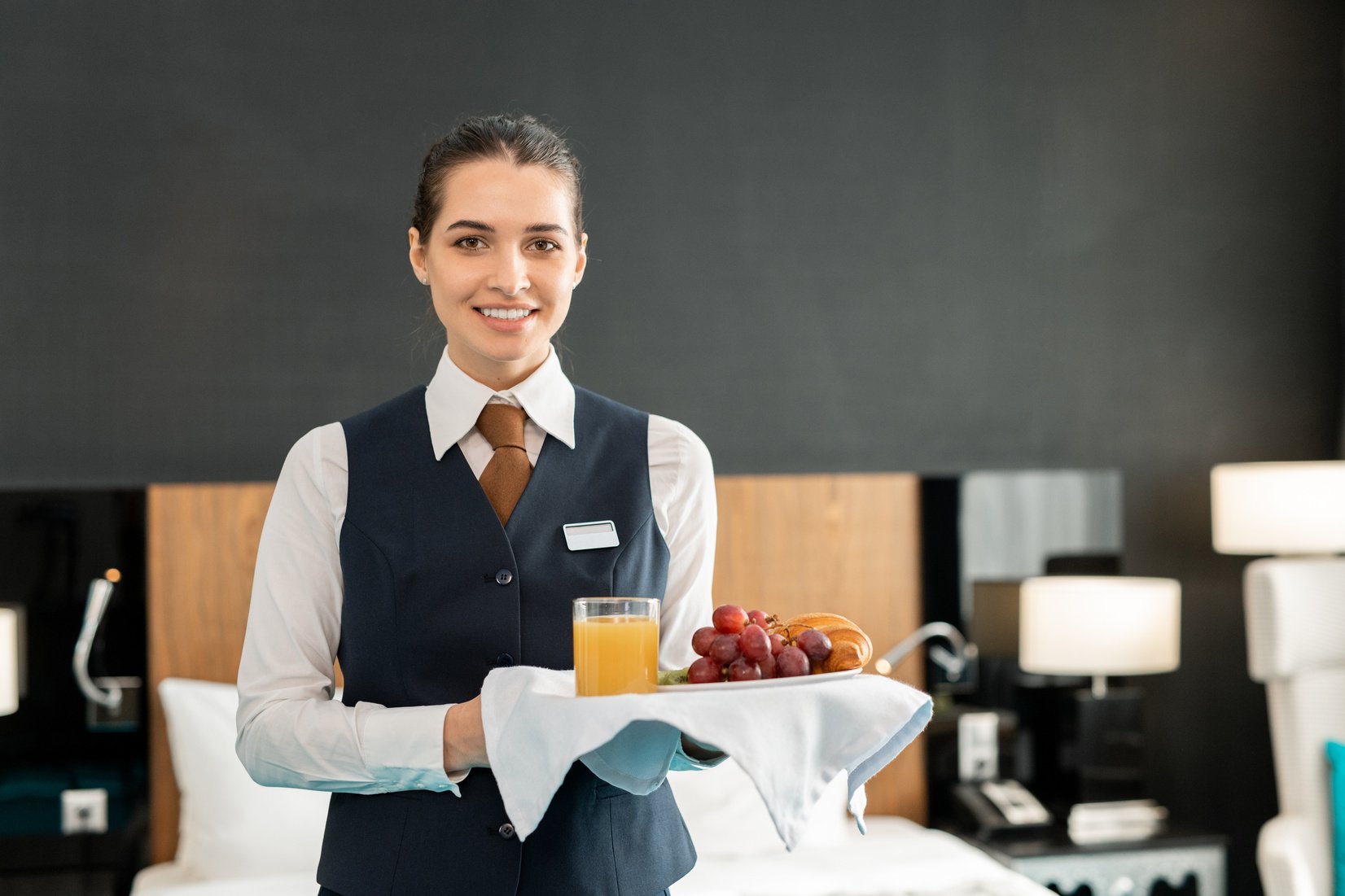 Young smiling hotel staff holding tray with breakfast